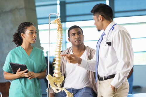 Photo of medical staff talking with a patient and showing a model of the spine