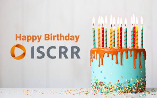 A teal and orange birthday cake with lots of candles and sprinkles sits next to text saying "Happy birthday ISCRR"